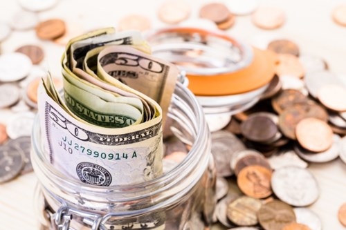 A jar full of dollar bills surrounded by coins